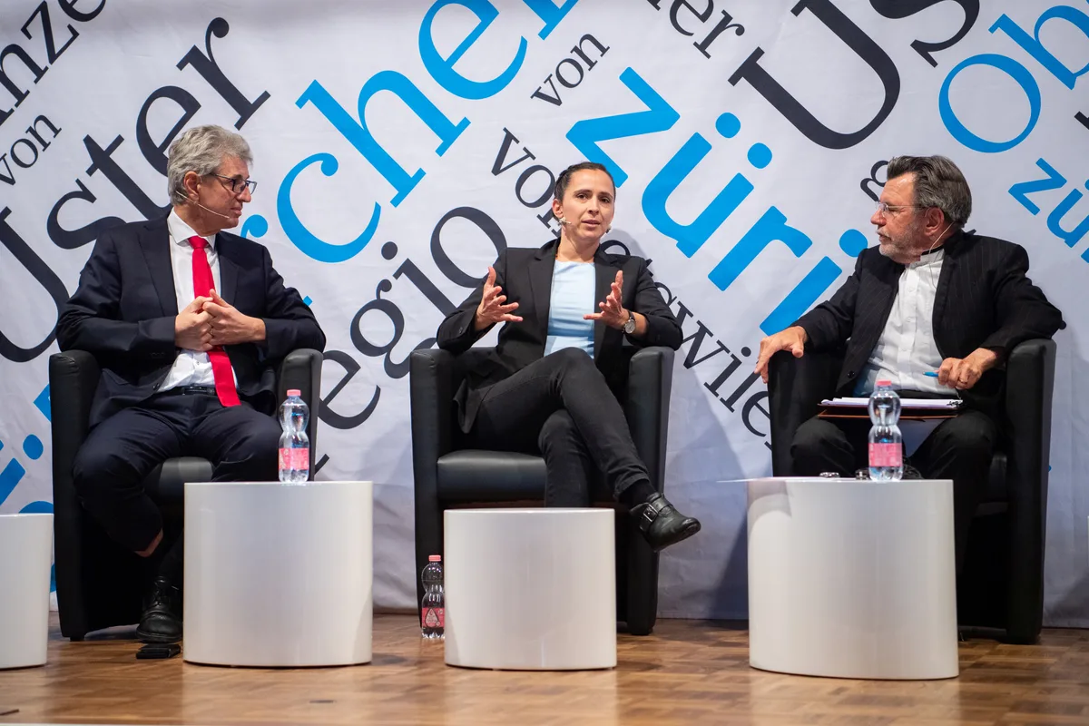 Drei Personen sitzen auf einer Bühne und diskutieren.